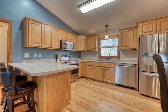 kitchen featuring stainless steel appliances, lofted ceiling, light brown cabinetry, a sink, and a peninsula