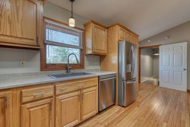 kitchen with light wood-style flooring, hanging light fixtures, vaulted ceiling, stainless steel appliances, and a sink