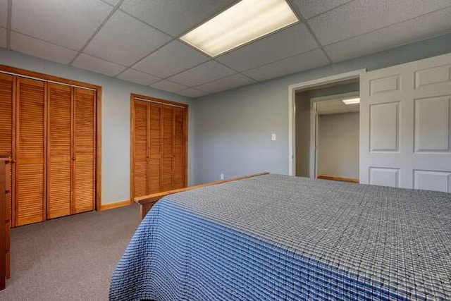 unfurnished bedroom with carpet, a paneled ceiling, baseboards, and two closets