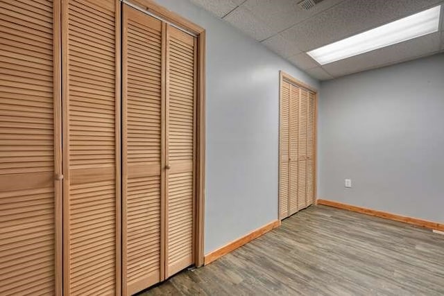 unfurnished bedroom with a paneled ceiling, two closets, baseboards, and wood finished floors