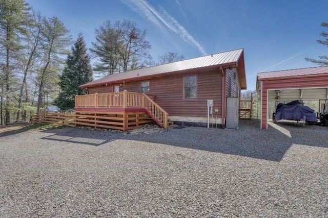 rear view of property featuring a deck, metal roof, and fence