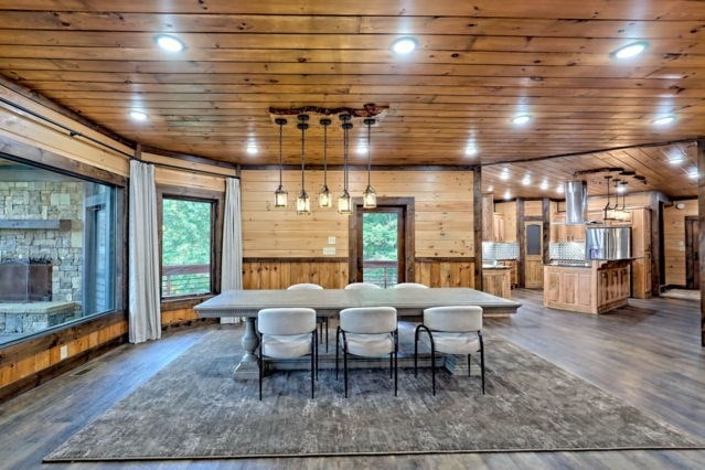 dining room featuring wooden walls, a stone fireplace, wood ceiling, and dark hardwood / wood-style floors