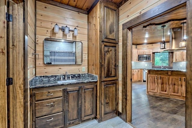 bathroom featuring decorative backsplash, wood ceiling, sink, and wooden walls