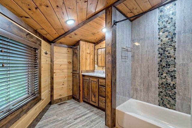 bathroom featuring vaulted ceiling, wood walls, wooden ceiling, and wood-type flooring