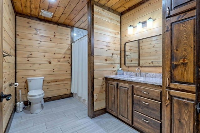 bathroom featuring wooden walls, walk in shower, vanity, wood ceiling, and toilet