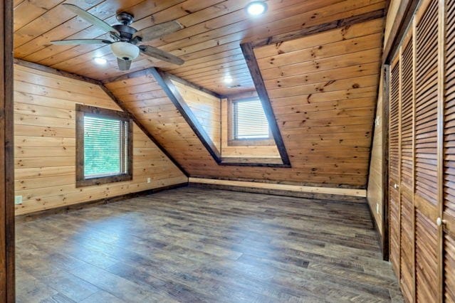 additional living space with wooden walls, vaulted ceiling with skylight, dark hardwood / wood-style flooring, and wooden ceiling