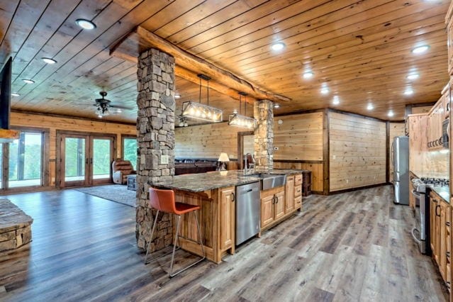 kitchen with wood walls, decorative light fixtures, hardwood / wood-style flooring, stainless steel appliances, and ornate columns