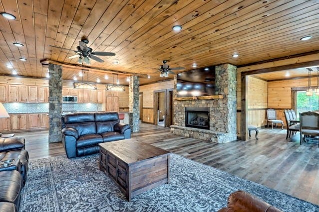 living room with wooden ceiling, dark hardwood / wood-style flooring, wooden walls, and a stone fireplace