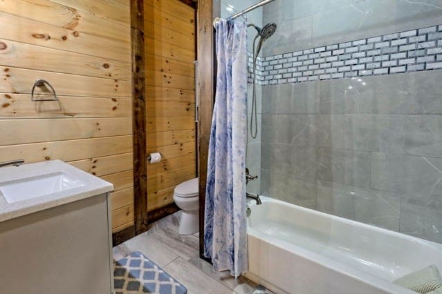 full bathroom with shower / tub combo with curtain, vanity, wooden walls, and toilet