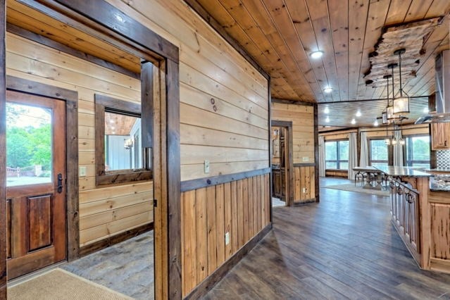 hall with a chandelier, dark wood-type flooring, wood walls, and wood ceiling