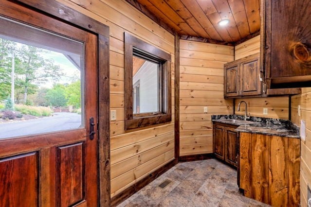 kitchen featuring wooden walls, sink, dark stone counters, and wooden ceiling