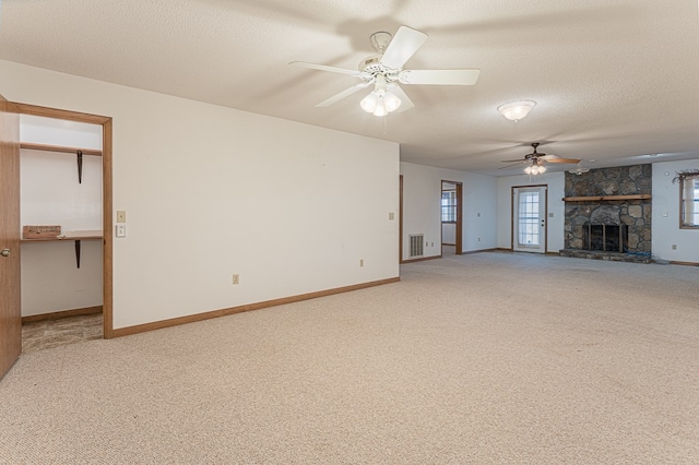 unfurnished living room featuring carpet, ceiling fan, a fireplace, and a textured ceiling