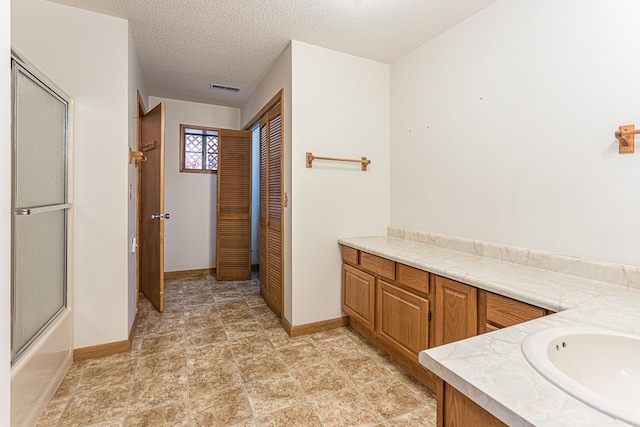 bathroom with vanity, bath / shower combo with glass door, and a textured ceiling