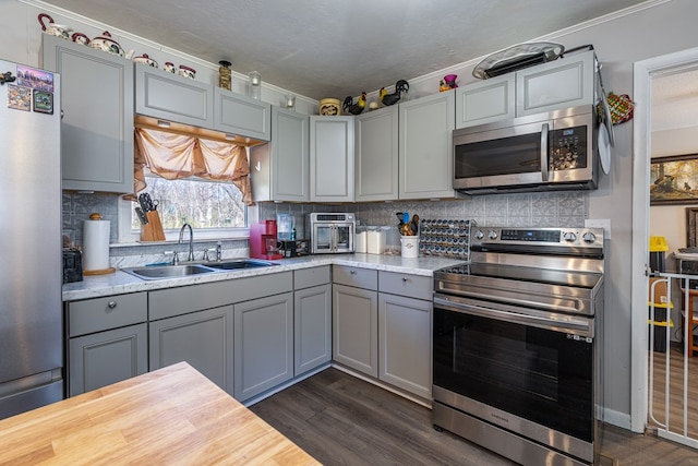 kitchen with stainless steel appliances, a sink, gray cabinets, ornamental molding, and dark wood-style flooring