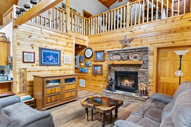 living room with a high ceiling, a stone fireplace, wood walls, and light hardwood / wood-style flooring