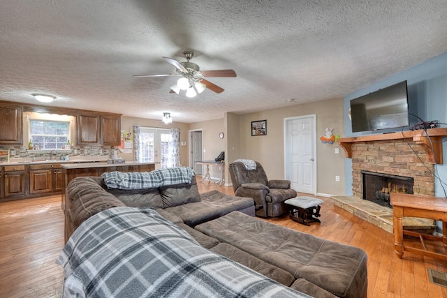 living room with sink, a stone fireplace, light hardwood / wood-style flooring, and a textured ceiling