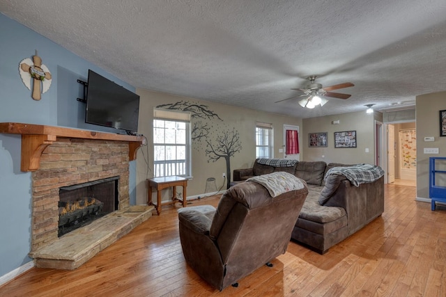 living room featuring a fireplace, light hardwood / wood-style flooring, a textured ceiling, and ceiling fan