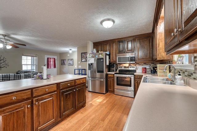 kitchen with sink, tasteful backsplash, a textured ceiling, appliances with stainless steel finishes, and light hardwood / wood-style floors