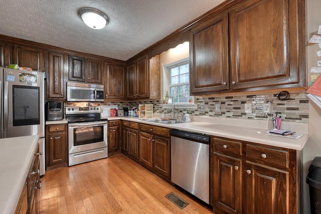 kitchen with sink, a textured ceiling, stainless steel appliances, light hardwood / wood-style floors, and backsplash