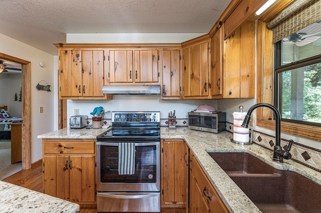 40 White Cloud Dr, Murphy, NC 28906 - kitchen featuring appliances with stainless steel finishes, under cabinet range hood, brown cabinetry, a textured ceiling, and light stone counters