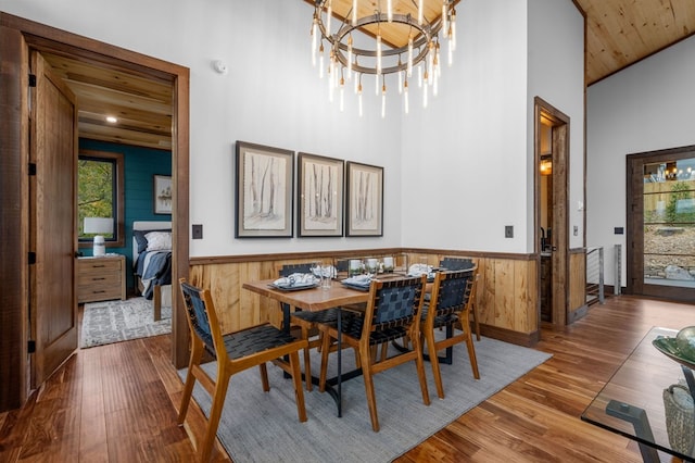 dining space featuring a chandelier, wood walls, wainscoting, wood finished floors, and high vaulted ceiling