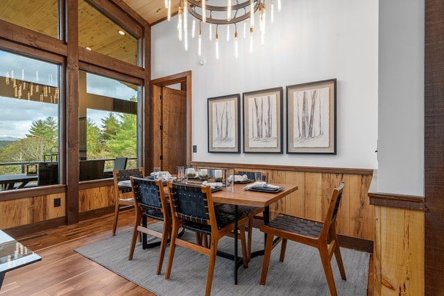 dining space featuring wooden walls, a notable chandelier, wood finished floors, and a wainscoted wall