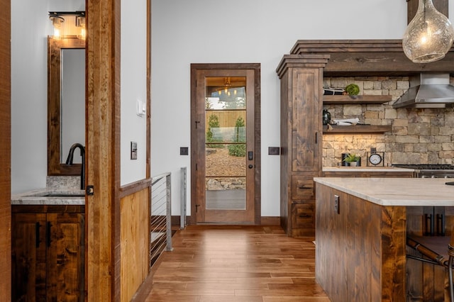 bar with a sink, light wood finished floors, pendant lighting, and wall chimney range hood