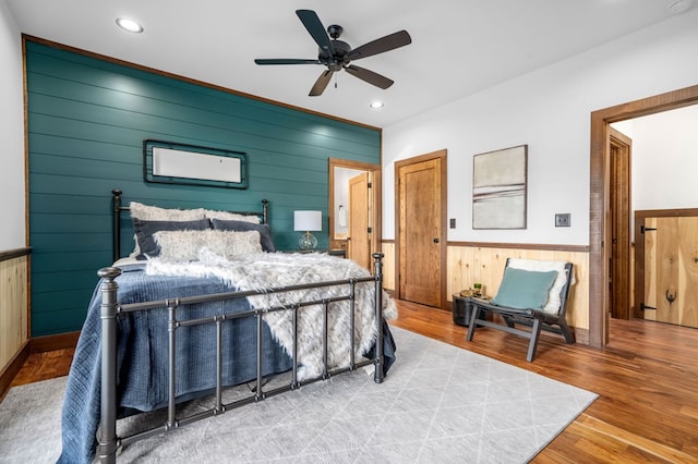 bedroom with a wainscoted wall, wood walls, recessed lighting, wood finished floors, and a ceiling fan