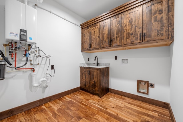 clothes washing area featuring baseboards, tankless water heater, light wood-style floors, cabinet space, and electric dryer hookup