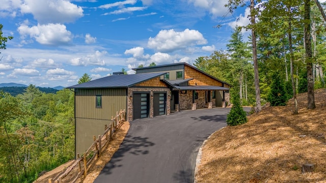 view of front of property featuring a forest view, aphalt driveway, and an attached garage