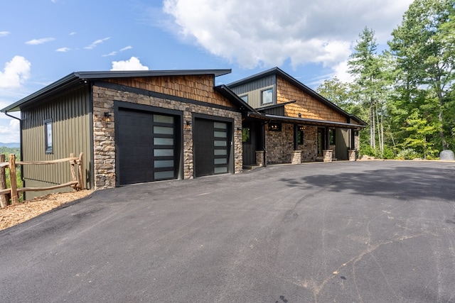 view of front of home featuring a garage, stone siding, fence, and aphalt driveway