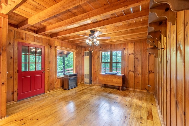 interior space with plenty of natural light, wooden walls, beamed ceiling, and a wood stove