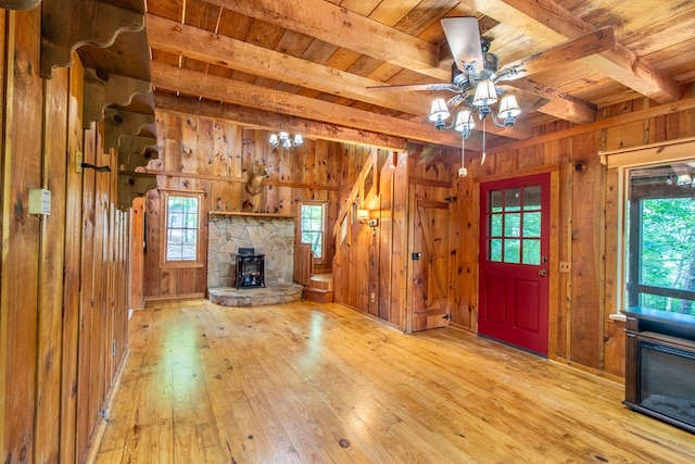 unfurnished living room with wooden ceiling, wooden walls, beam ceiling, and a wood stove