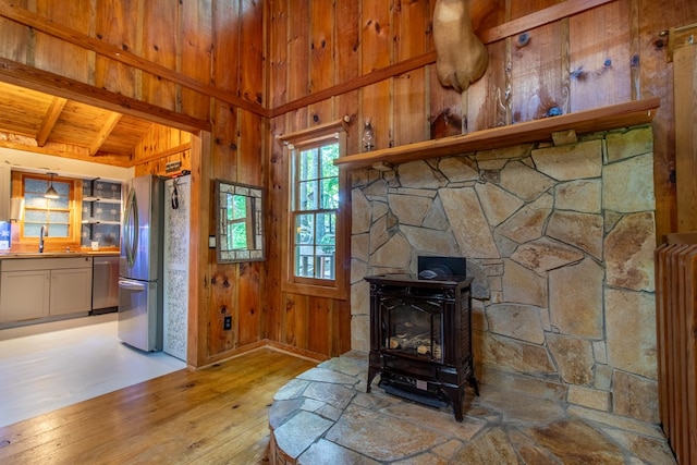 interior space featuring sink, wooden walls, stainless steel appliances, beamed ceiling, and a wood stove