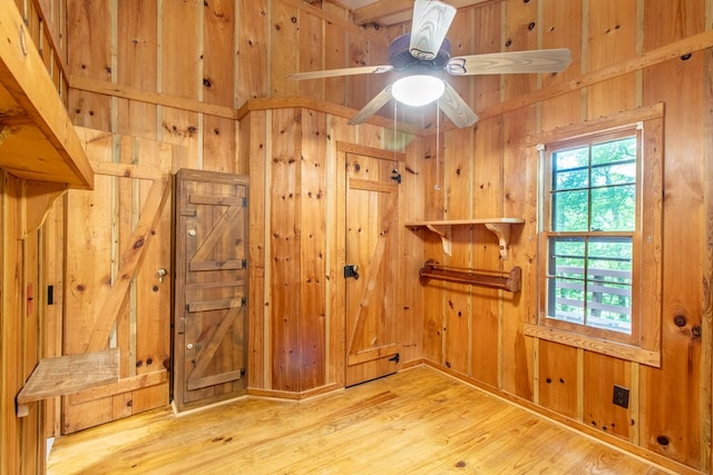 interior space featuring ceiling fan, wooden walls, and light hardwood / wood-style floors