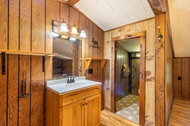 bathroom with vanity, hardwood / wood-style floors, vaulted ceiling, and wood walls