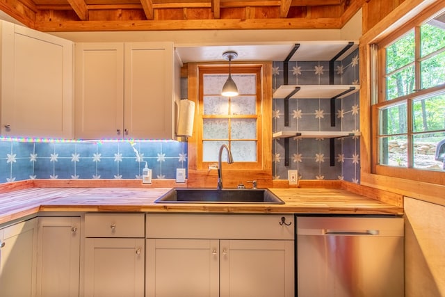 kitchen with sink, dishwasher, white cabinetry, hanging light fixtures, and wood counters