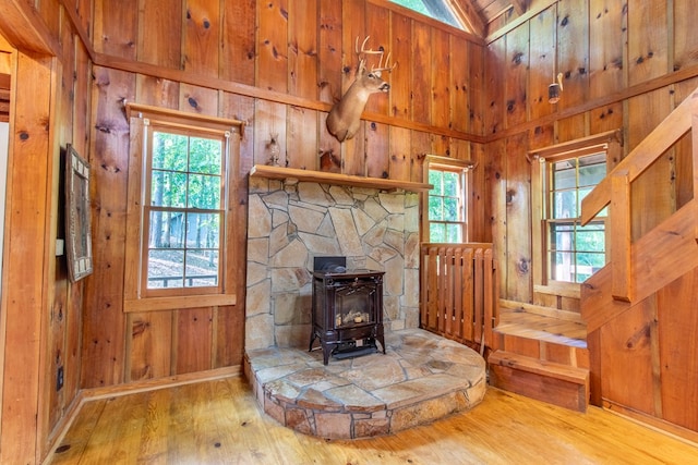 unfurnished living room with wood-type flooring, a wood stove, a wealth of natural light, and wood walls