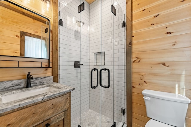 bathroom featuring toilet, a stall shower, wooden walls, and vanity