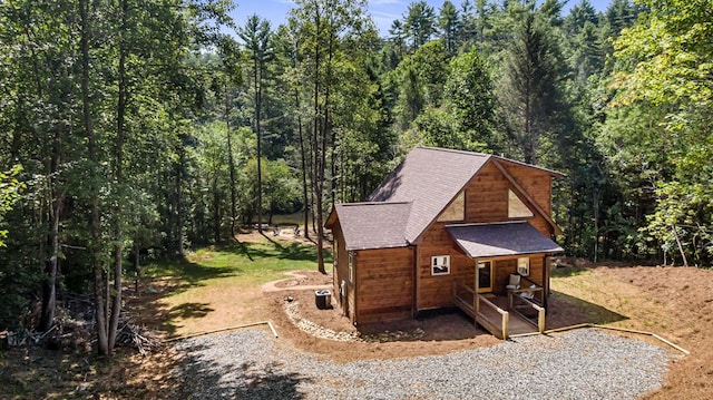 view of side of property featuring covered porch, a forest view, roof with shingles, and cooling unit