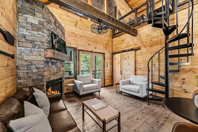 unfurnished living room featuring a stone fireplace, a barn door, wood walls, stairway, and hardwood / wood-style floors