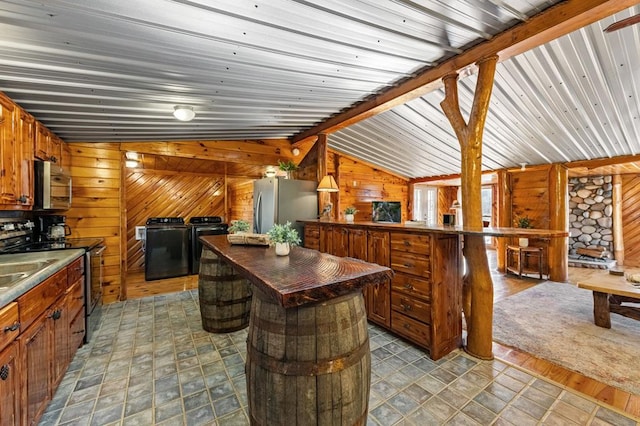 kitchen with wood walls, lofted ceiling with beams, a kitchen island, stainless steel appliances, and washing machine and dryer