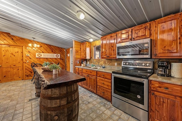 kitchen featuring stainless steel appliances, sink, wood walls, and decorative backsplash