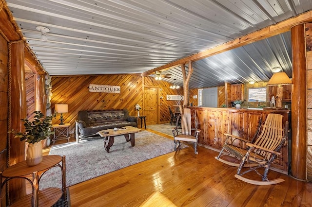 living area with wood-type flooring, lofted ceiling with beams, and wooden walls