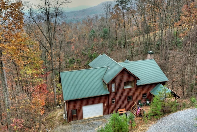 exterior space with gravel driveway, a chimney, a forest view, and metal roof