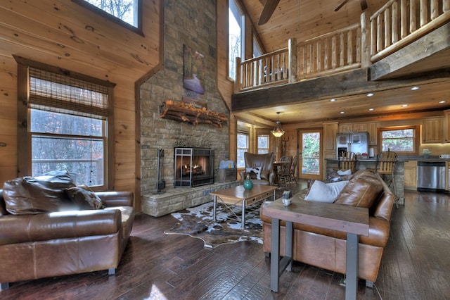 living room featuring wooden walls, wood-type flooring, a stone fireplace, and a high ceiling