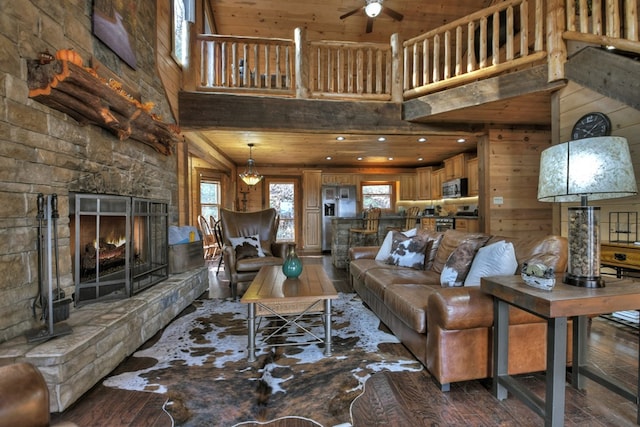 living room featuring hardwood / wood-style floors, a stone fireplace, a high ceiling, and wood walls