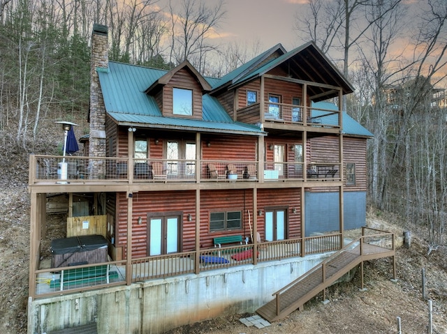 back house at dusk with a balcony and a hot tub