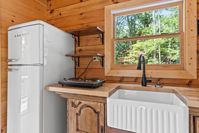 kitchen with wooden walls, white refrigerator, sink, and wooden counters