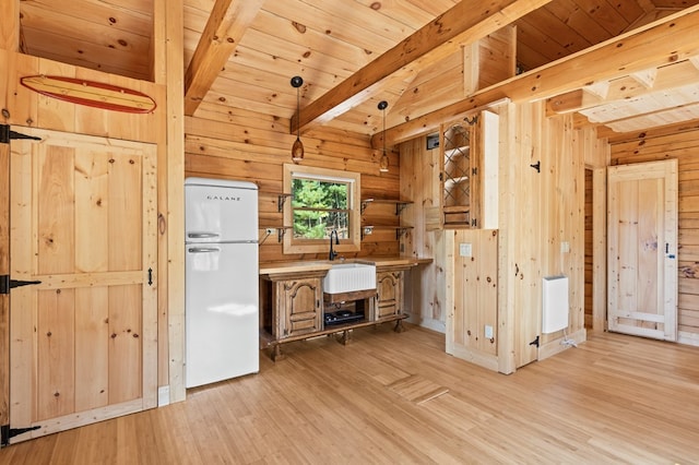 kitchen featuring light hardwood / wood-style floors, wood walls, white refrigerator, and hanging light fixtures